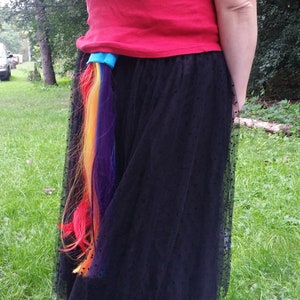 May include: A black tulle skirt with a rainbow colored hair extension attached to the back.