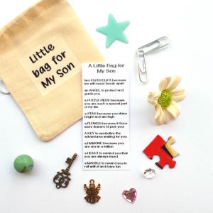 Peut inclure: Un petit sac en toile de jute rempli de divers petits objets, dont une étoile, une pièce de puzzle, une clé, un cœur, une bille et une figurine d'ange. Le sac est étiqueté "Un petit sac pour mon fils" et comprend un poème sur la signification de chaque objet.