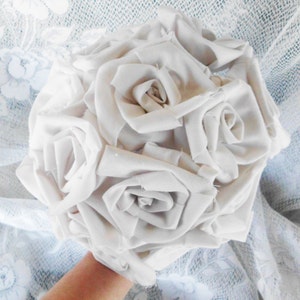 May include: A bouquet of white fabric roses, arranged in a circular shape. The roses are made from a soft, white fabric and have a realistic appearance.