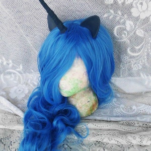 May include: A blue wig with a black unicorn horn and ears. The wig is styled in loose curls and is on a mannequin head.