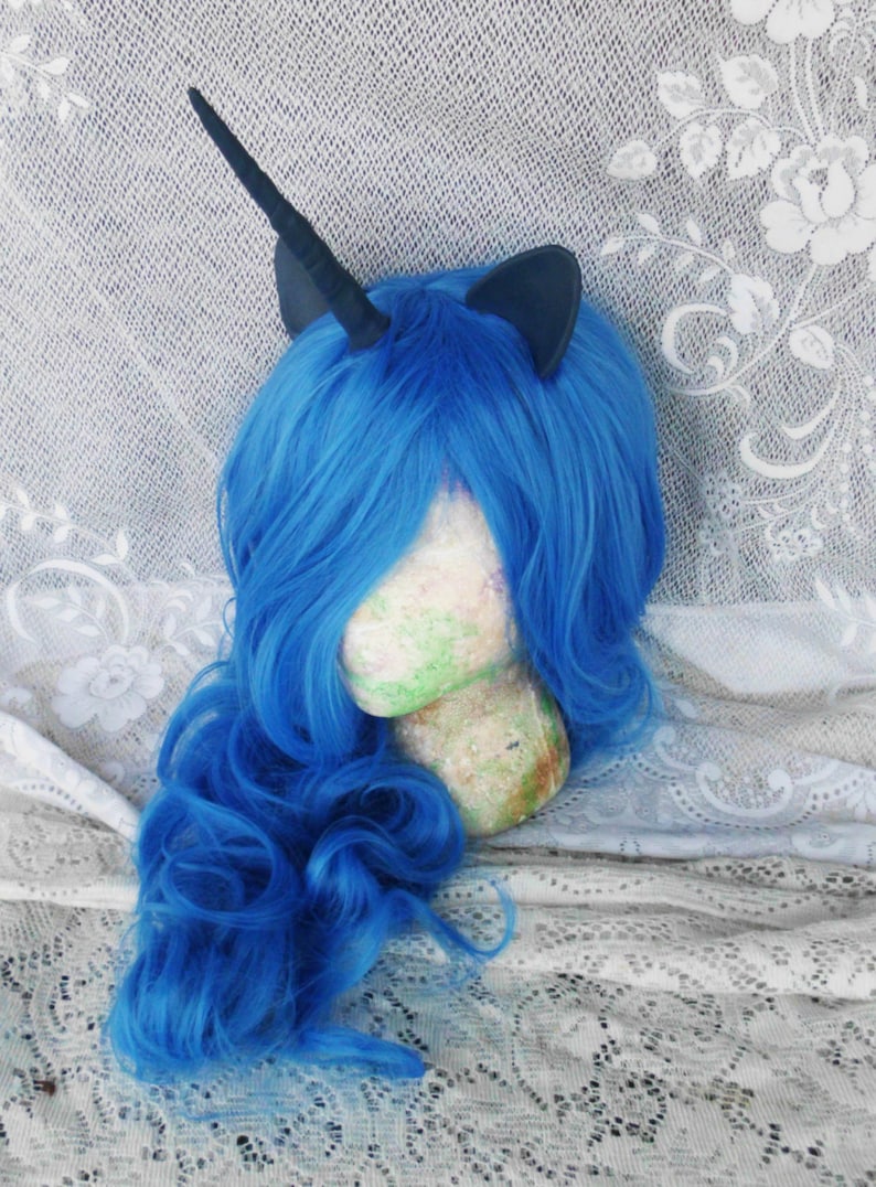 May include: A blue wig with a black unicorn horn and ears. The wig is styled in loose curls and is on a mannequin head.