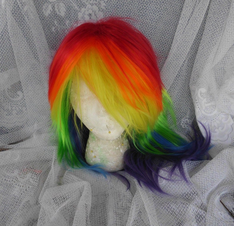 May include: Rainbow colored wig with long, straight hair. The wig is styled with a side part and the hair is layered. The wig is on a mannequin head.