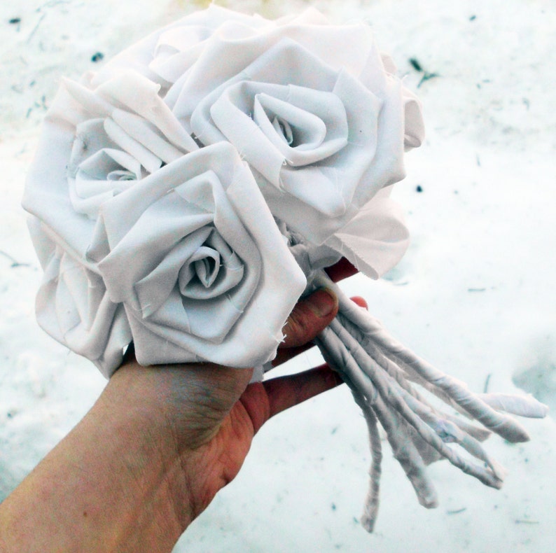 May include: A bouquet of white fabric roses, tied together with fabric stems.