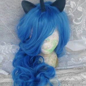 May include: A blue wig with a black unicorn horn and ears. The wig is styled in loose curls and is on a mannequin head.