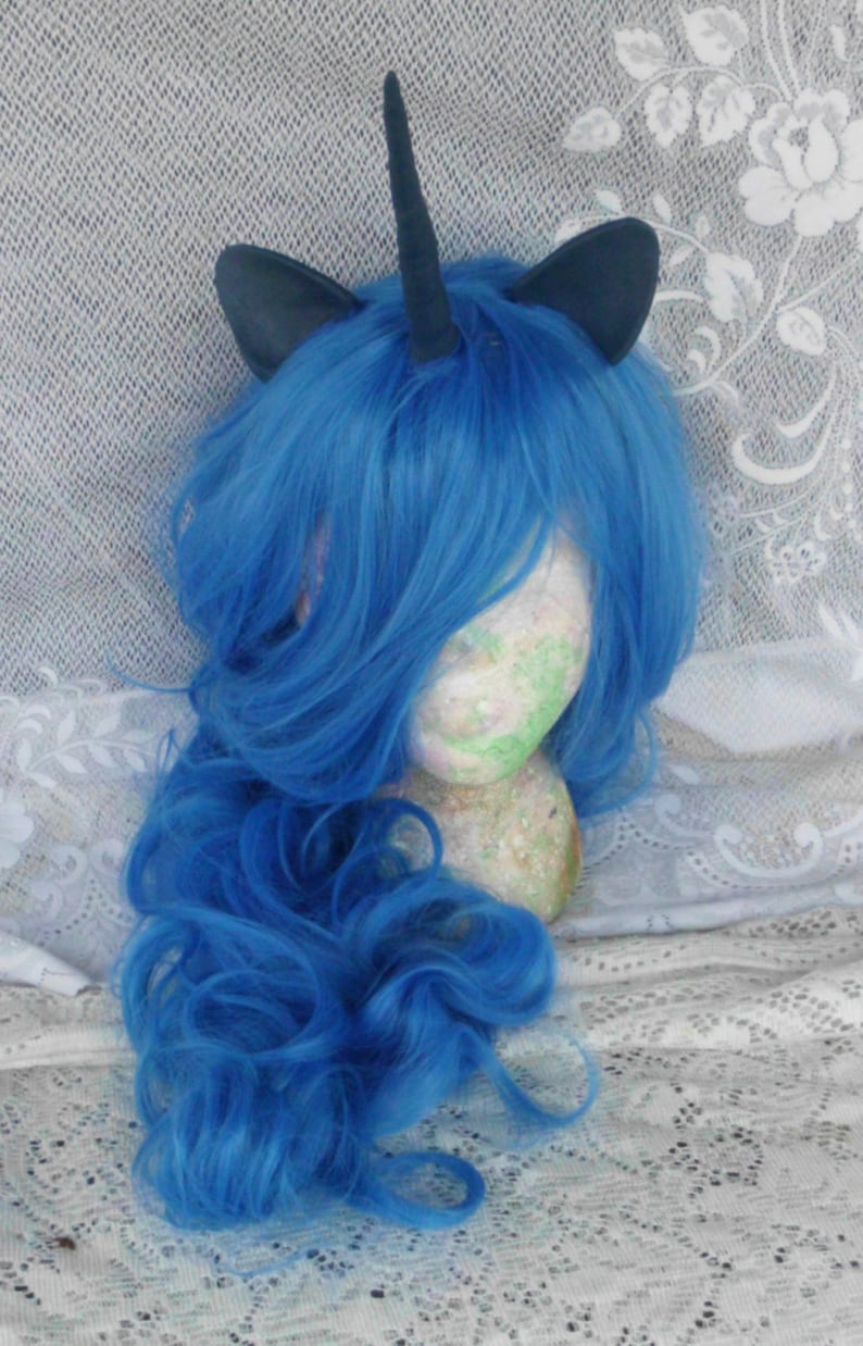 May include: A blue wig with a black unicorn horn and ears. The wig is styled in loose curls and is on a mannequin head.