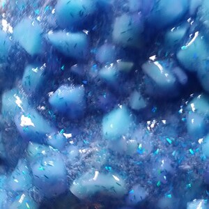 Puede incluir: Primer plano de slime azul con purpurina iridiscente. La slime est&aacute; llena de peque&ntilde;as piezas azules transl&uacute;cidas.