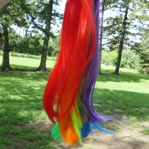 May include: A rainbow-colored hair extension with red, orange, yellow, green, blue, and purple strands. The extension is made of synthetic hair and is about 12 inches long.