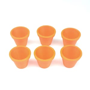May include: Six small, terracotta-colored flower pots are arranged on a white surface. The pots are empty, with a simple, rounded design. The pots are suitable for small plants or succulents.