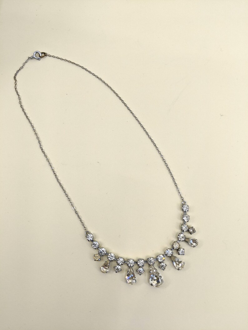 Puede incluir: Un collar de cadena de plata con un colgante de cristal en forma de l&aacute;grima. El colgante est&aacute; rodeado de cristales m&aacute;s peque&ntilde;os.