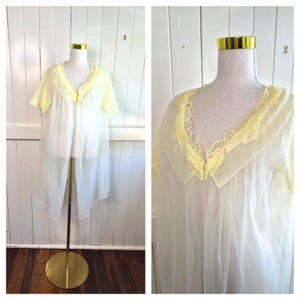 May include: A vintage, sheer, white and yellow negligee displayed on a mannequin. The negligee features a yellow lace trim around the neckline and sleeves. The garment is open in the front and has a flowing, lightweight design.