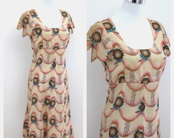 May include: A cream-colored midi dress featuring a repeating pattern of brown sunflowers with blue leaves, accented by wavy pink scalloped lines. The garment has a scoop neckline and short, fluttery sleeves, displayed on a mannequin torso.