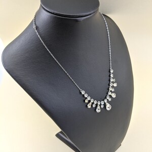 Puede incluir: Un collar de cadena de plata con un colgante de cristal en forma de l&aacute;grima. El colgante est&aacute; rodeado de cristales m&aacute;s peque&ntilde;os, creando un efecto en cascada.
