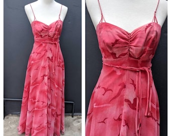 May include: A floor-length dress in shades of pink and red featuring a repeating bird silhouette pattern. The garment has thin spaghetti straps, a sweetheart neckline with gathered fabric at the center, and a matching tie belt at the waist.