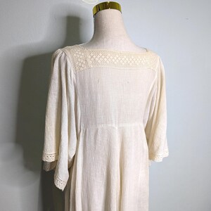 May include: Cream-colored dress with a square neckline and three-quarter sleeves. The dress features a delicate lace yoke and lace trim on the sleeves. The fabric has a subtle textured appearance, and the dress has a flowing, relaxed fit.