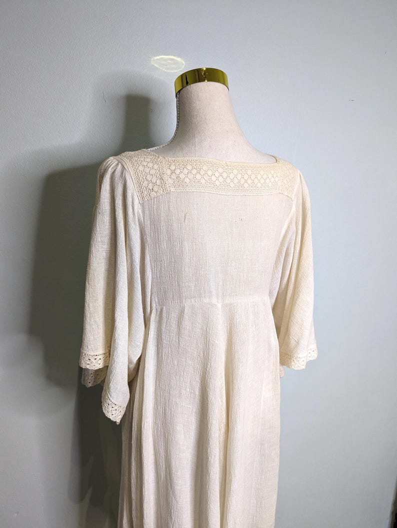 May include: Cream-colored dress with a square neckline and three-quarter sleeves. The dress features a delicate lace yoke and lace trim on the sleeves. The fabric has a subtle textured appearance, and the dress has a flowing, relaxed fit.