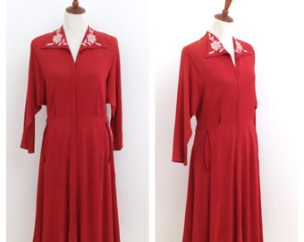May include: A red vintage dress with a white floral embroidered collar and a zipper closure. The dress has a fitted bodice and a flared skirt.