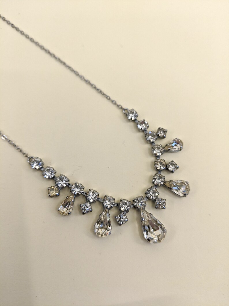 Puede incluir: Un collar de cadena de plata con un colgante de cristal en forma de l&aacute;grima. El colgante est&aacute; rodeado de cristales m&aacute;s peque&ntilde;os.
