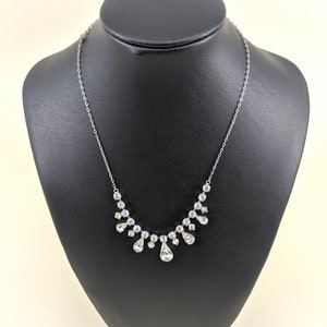 Puede incluir: Un collar de cadena de plata con un colgante de cristal en forma de l&aacute;grima y cristales m&aacute;s peque&ntilde;os dispuestos en forma de cascada.