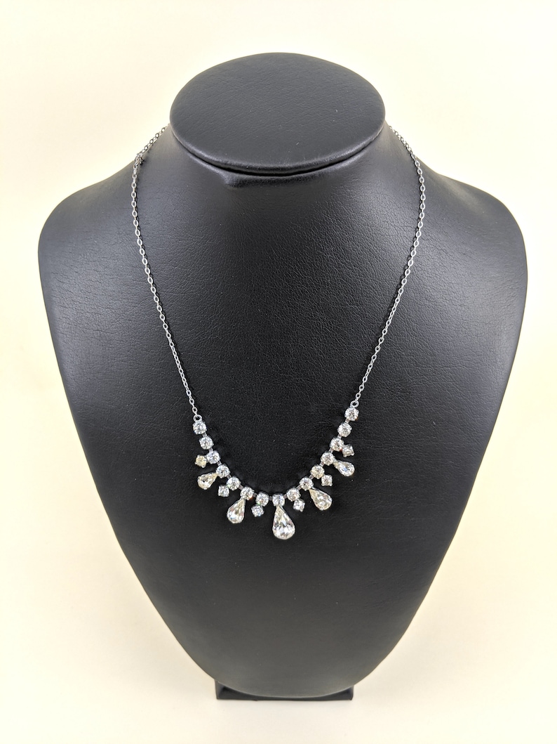Puede incluir: Un collar de cadena de plata con un colgante de cristal en forma de l&aacute;grima y cristales m&aacute;s peque&ntilde;os dispuestos en forma de cascada.