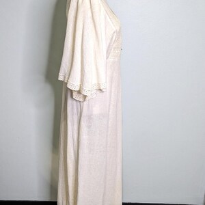 May include: Off-white vintage maxi dress with flared sleeves and a V-neckline. The dress features delicate lace trim on the sleeves and neckline. The dress is displayed on a gold dress form.