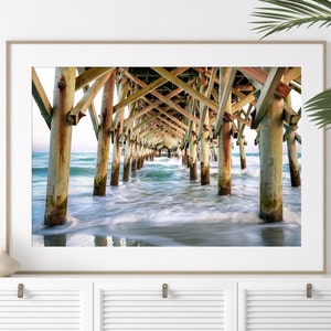 PHotography print of underneath a pier with small waves.  Pier is wooden with teal blue water.