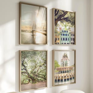 May include: Four framed art prints with landscape scenes. The prints feature a bridge, colourful buildings, a large tree, and a fountain. Each print is in a light-coloured wooden frame, displayed on a white wall.