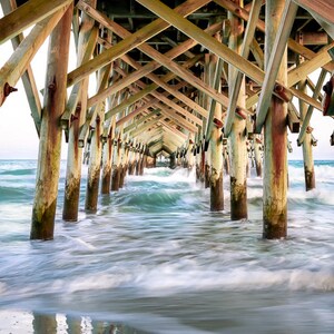 PHotography print of underneath a pier with small waves.  Pier is wooden with teal blue water.