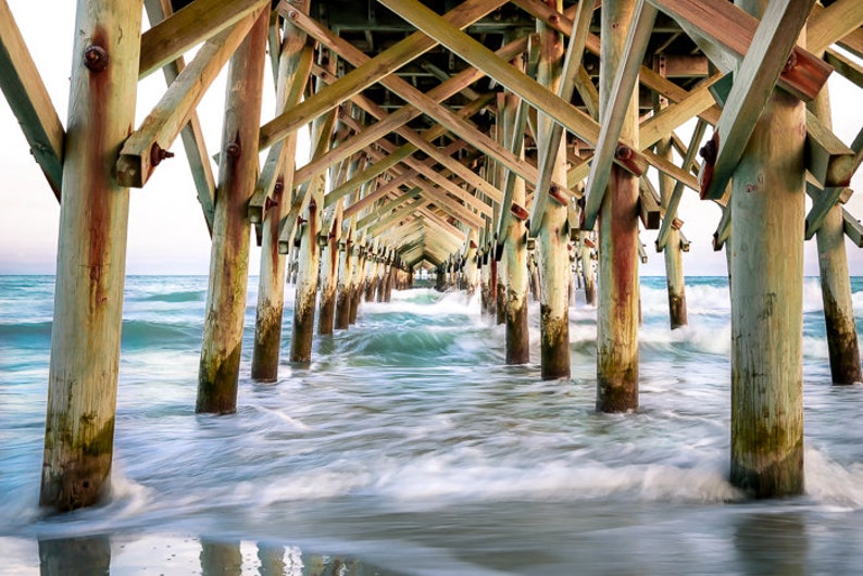 PHotography print of underneath a pier with small waves.  Pier is wooden with teal blue water.