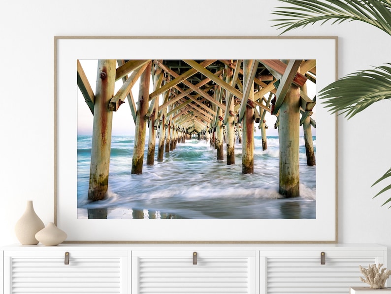 PHotography print of underneath a pier with small waves.  Pier is wooden with teal blue water.