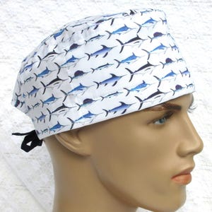 May include: White surgical scrub cap with a repeating pattern of blue and black marlin fish. The cap has a black tie in the back. The cap is made of a soft, lightweight fabric.