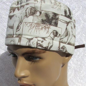 May include: A white scrub hat with a brown and white print of hunting dogs. The hat has a brown adjustable tie.