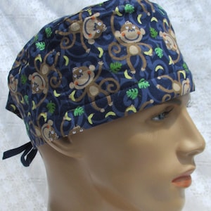 May include: A blue scrub hat with a pattern of brown monkeys swinging from vines and yellow bananas. The monkeys have brown fur and white faces.