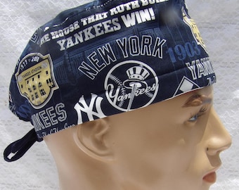 May include: A navy blue Yankees baseball cap with white text and graphics. The cap features the text "NEW YORK", "YANKEES WIN!", and "YANKEE STADIUM". The cap has a tie in the back.