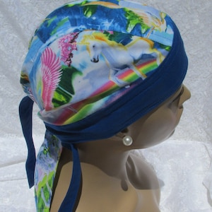 May include: A blue and white patterned bandana with a unicorn and rainbow design. The bandana is tied around a person's head and has a blue trim.