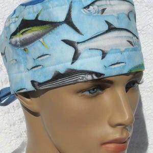 May include: A blue surgical scrub hat with a colorful print of various fish. The hat has a tie on the back.