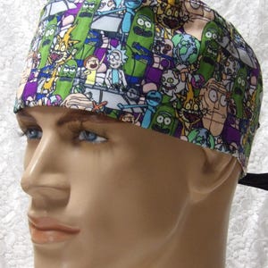 May include: A patterned surgical scrub cap featuring cartoon characters in green, purple, and blue. The cap is tied in the back with a black tie. The cap is worn by a mannequin.