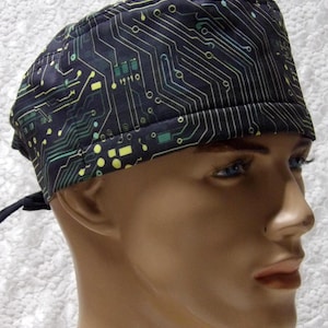 May include: A dark blue surgical scrub cap with a repeating circuit board pattern in shades of green, yellow, and white. The cap is tied in the back with black ties. The cap is worn by a mannequin.
