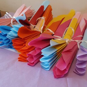 May include: A stack of colorful tissue paper fans tied with white ribbon. The fans are in shades of pink, orange, yellow, blue, and purple.