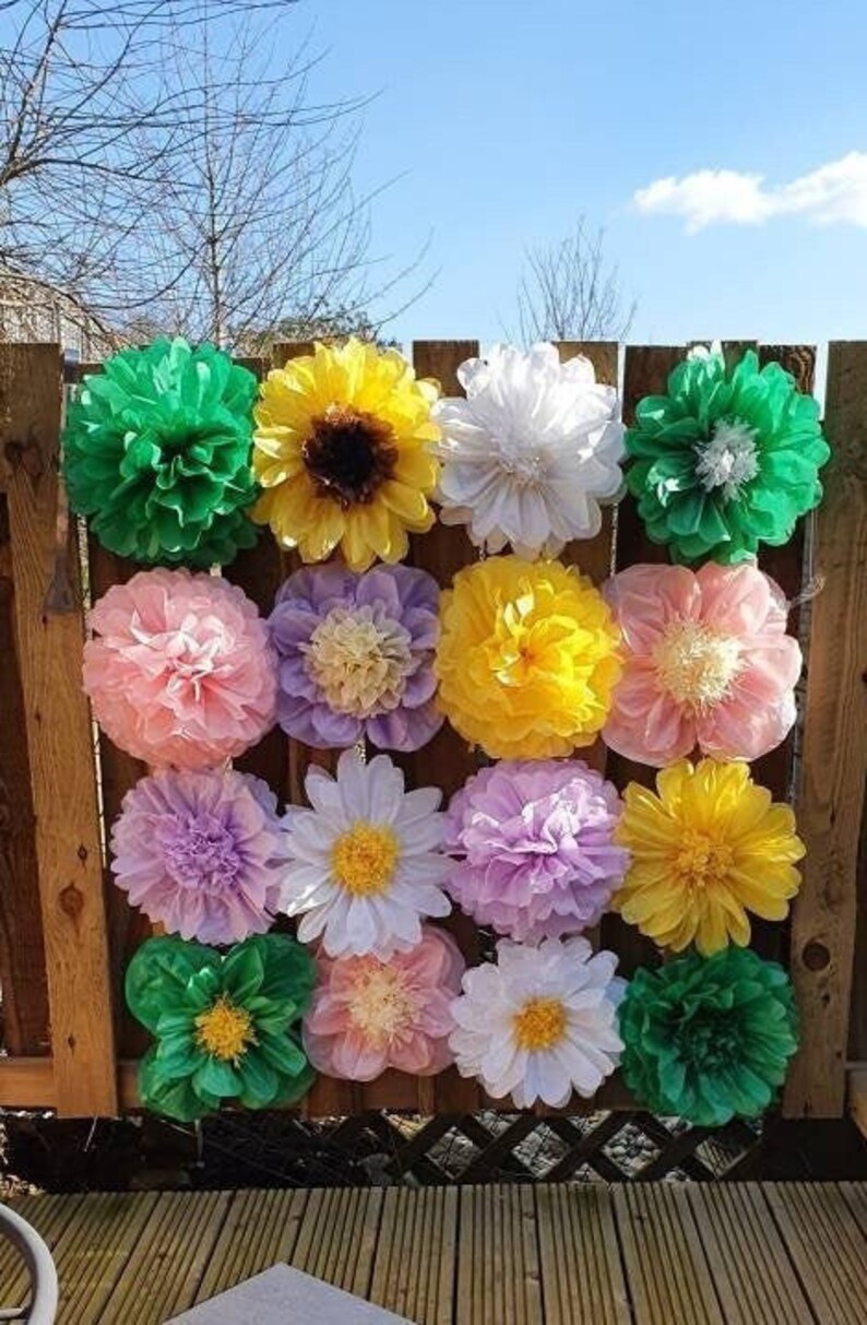 May include: A wall decorated with tissue paper flowers in various colors, including pink, yellow, green, white, and purple. The flowers are arranged in a grid pattern and are all the same size.