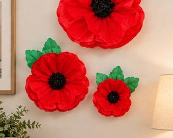 May include: Three decorative wall art flowers made of red paper with ruffled petals, black centers, and green paper leaves. The flowers are arranged in a cluster on a wall, featuring one large, one medium, and one small poppy-style blossom.