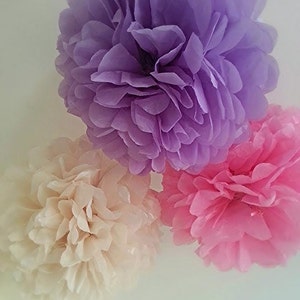May include: Three tissue paper pom-poms in different shades of pink and purple. The pom-poms are a popular decoration for parties and events.