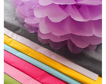 May include: A stack of colorful tissue paper in shades of green, pink, red, blue, yellow, and white. The tissue paper is layered on top of a gray sheet of tissue paper. A large purple tissue paper flower is on top of the stack.