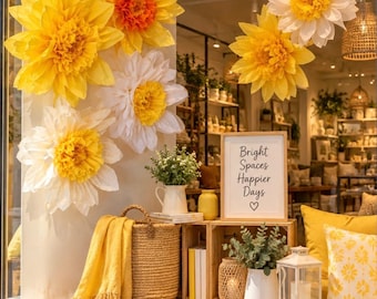 Könnte beinhalten: Ein Schaufenster mit großen Papierblumen in Gelb und Weiß, einem geflochtenen Korb mit gelber Decke, einem Schild mit der Aufschrift Bright Spaces Happier Days, einem weißen Krug mit Grünpflanzen, einer Laterne und gelben Kissen mit Muster.