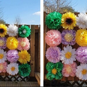 May include: A wall decorated with tissue paper flowers in various colors, including green, yellow, white, pink, and purple. The flowers are arranged in a grid pattern and are attached to a wooden fence.