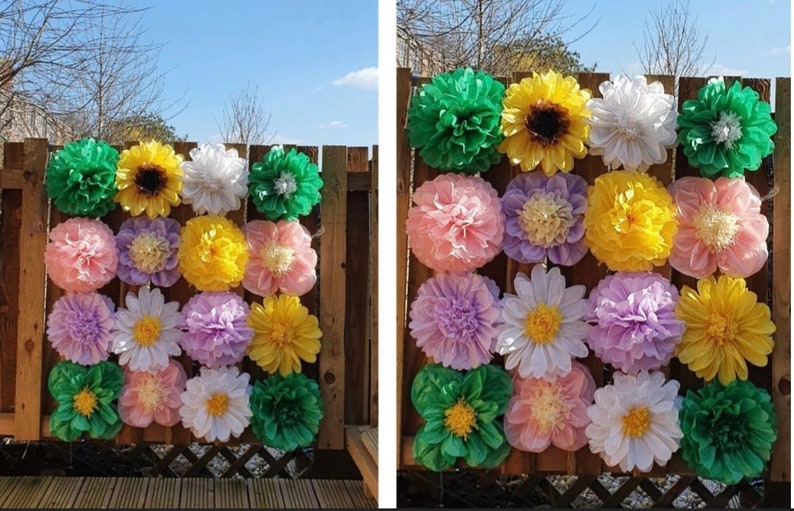 May include: A wall decorated with tissue paper flowers in various colors, including green, yellow, white, pink, and purple. The flowers are arranged in a grid pattern and are attached to a wooden fence.