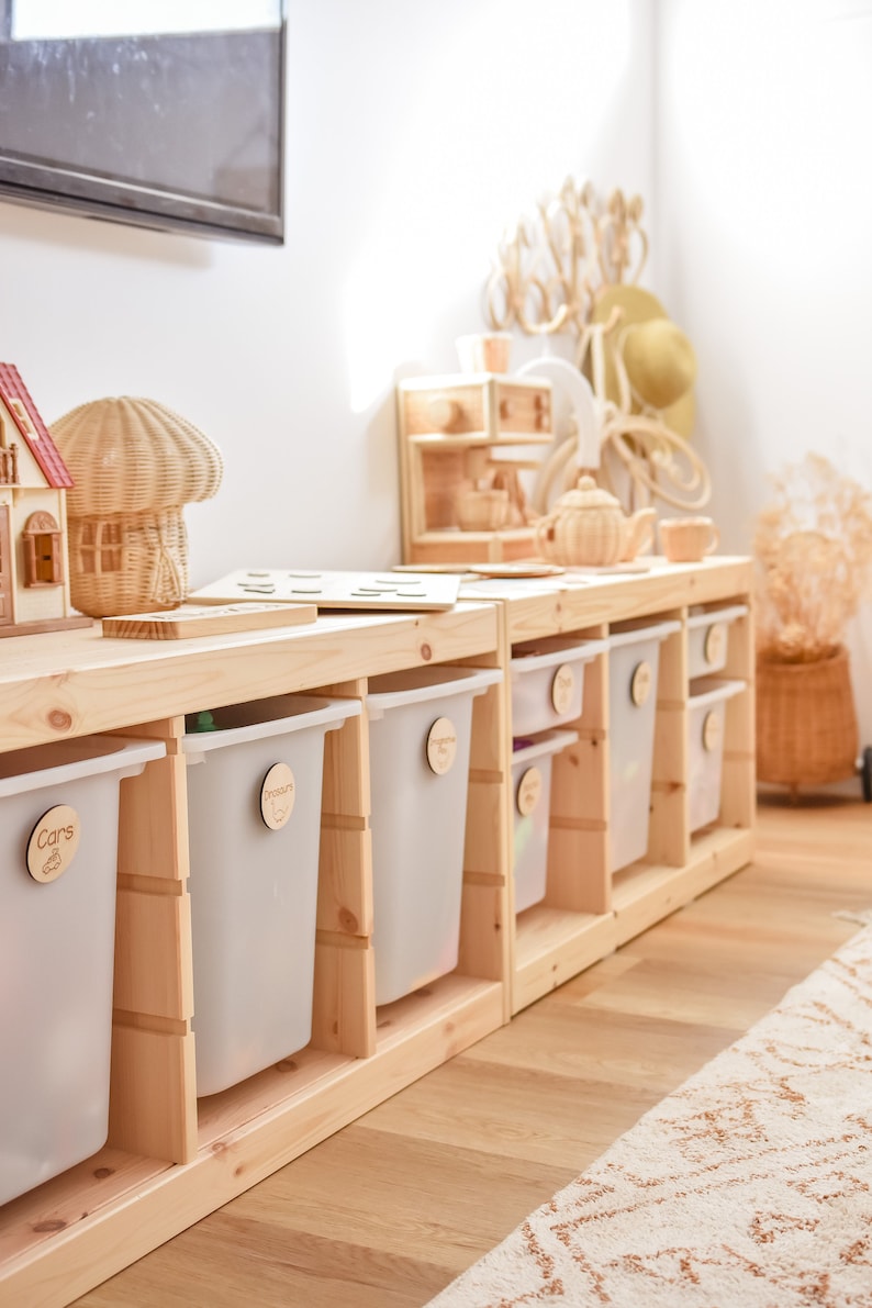 May include: A wooden storage unit with six clear plastic bins. The bins are labeled with wooden tags that say "Cars", "Dinosaurs", "Blocks", "Books", "Puzzles", and "Art".