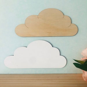 Op de afbeelding: Twee houten wolkvormen, een wit geschilderd en een in zijn natuurlijke houtkleur gelaten. De wolken bevinden zich op een lichtblauwe achtergrond.