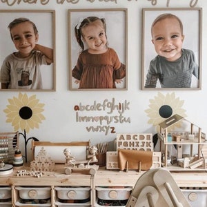 May include: A playroom with a wooden table and storage bins. The wall is decorated with a wooden sign that says "Where the wild ones play" and a wooden alphabet. There are three framed photos of children on the wall.