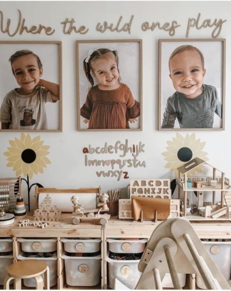 May include: A playroom with a wooden table and storage bins. The wall is decorated with a wooden sign that says "Where the wild ones play" and a wooden alphabet. There are three framed photos of children on the wall.