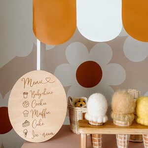 May include: A wooden sign with a menu for a pretend ice cream shop. The menu lists: Babychino, Cookie, Muffin, Cake, and Ice Cream. There are four felt ice cream cones on a wooden stand.